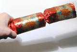 Male hand holding a colorful red Christmas cracker table decoration ready to pull it with a friend over a white background