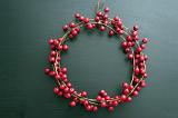 Red cranberry circular berry wreath for Christmas over a drak background with copy space for a seasonal greeting