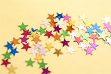 Scattering of festive multicolored stars on a yellow background for your Christmas or seasonal greeting