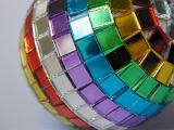 Unusual vibrant multicolored festive bauble with rows of tiny mosaics in the colours of the rainbow, close up view for a colorful Christmas or holiday background