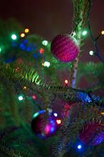 Glitter baubles on a natural evergreen Christmas tree in shades of magenta and purple with sparkling festive colorful lights shining in the darkness