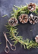 Making homemade Christmas decorations with scissors alongside a half completed pine wreath with cones viewed from above
