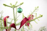 Minimalist decorated Christmas tree with single green bauble and colorful red ribbon adorning the branches
