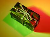 Small rectangular gift box wrapped in decorative shiny green paper and tied with a golden cord, close-up with shadow and copy space