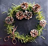 Rustic handmade Christmas wreath of natural pine foliage and cones over a dark textured background with a pair of scissors