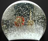 Christmas snow globe with suspended winter snow obscuring colorful red and gold buildings , close up view of the dome against a black background
