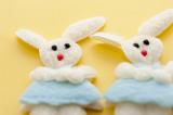 Two fluffy Easter bunnies in blue clothes, flat decorative needlework pieces on yellow