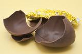 Broken chocolate Easter egg alongside its foil wrapping on a yellow background.