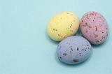 Three pastel coloured speckled candy Easter Eggs on blue with copyspace.