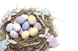 Straw nest filled with candy Easter eggs and with four fluffy needlework Easter bunnies on white