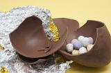 Large chocolate Easter egg broken in to pieces on the foil wrapper and filled with small speckled candy eggs.