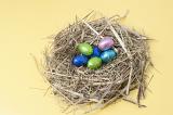 Colourful foil wrapped chocolate Easter Eggs in a straw nest on yellow background.