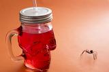 Red skull shaped Halloween drink in a glass Mason jar with lid and straw with scary spider below on a red background with copy space