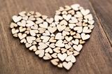 Heart-shaped pile of smaller wooden hearts, cut of unpainted plywood, close-up over wooden table surface background