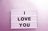 White lightbox with I Love You message sign of black changeable letters, against wall in purple lighting. Love concept
