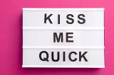 Kiss Me Quick message on white lightbox with black changeable letters, close-up over pink background