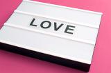 Changeable sign LOVE on white table box laying on pink background surface