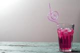 Glass of red beverage with ice and curved heart shaped pink cocktail drinking straw on old wooden table. Copy space