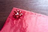 Cropped close-up image of present box wrapped with red glossy paper and decorated with ruby ribbon, on lacquered table. Romantic gift concept