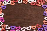 Valentines Day heart frame on wood with colorful cut out heart shapes arranged as border over a textured wooden background with woodgrain and copy space