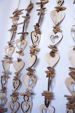 Unpainted wooden hearts strung on beading strings decoration hanging close to white wall. Close-up background concept