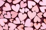 Background pattern of pink wooden hearts in three sizes arranged randomly on red in a concept of love, romance, anniversary, wedding or Valentines Day