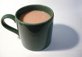 Close-up of a green porcelain mug full of hot coffee with milk, with shadow, on grey