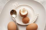 Three boiled eggs for breakfast with one with the top removed ready to eat in an eggcup and the other two lying alongside on the plate
