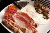 Wholesome cooked English breakfast with fried eggs, grilled bacon, sausages, mushrooms, plack pudding and tomato for a hearty diet