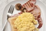 Scrambled egg on toast served with lean grilled bacon rashers and mushroom , close up view from above