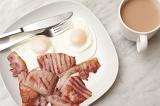 Serving of two fired eggs and tasty rashers of grilled bacon for breakfast with a cup of freshly brewed coffee