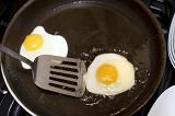 Frying eggs for breakfast in a teflon coated frying pan in hot oil using a metal lifter kitchen utensil