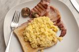 Scrambled eggs and bacon for a nourishing breakfast served on a slice of toast with a mushroom, view from above