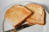 Two slices of hot buttered white toast for breakfast served with a knife on a side plate as an accompaniment to the meal
