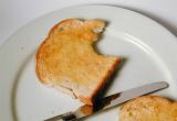 Slice of hot buttered white toast on a white plate for breakfast bitten into on the corner