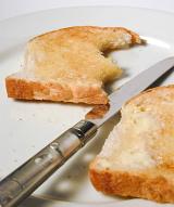 Buttered slices of white toast on a plate with a knife with one slice missing two bites