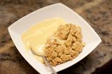 Serving of delicious apple crumble and custard for dessert in a modern square white bowl, high angle view of the crumbly topping