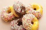 Assorted ring doughnuts with sprinkles and chocolate or orange icing in a random pile ready for a delicious coffee break