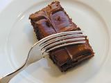 Eating a portion of delcious chocolate cake topped with decorative icing with a fork, close up view on a white plate