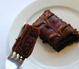 Mouthful of delicious fresh chocolate cake suspended on a fork above a served slice of glazed confectionery