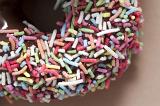 Background texture of a freshly baked decorated chocolate ring doughnut or donut covered in colorful sprinkles