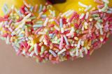 Fresh doughnut with orange icing dipped in colorful sprinkles with a close up view of the sprinkles
