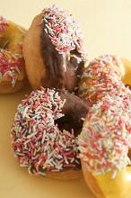 Pile of freshly baked glazed ring doughnuts decorated with colorful sprinkles, closeup side view