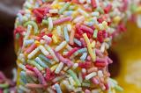 Texture detail of colorful candy sprinkles on a fresh lemon glazed ring doughnut served for a morning coffee break