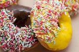 Batch of freshly baked glazed doughnuts or donuts with chocolate and lemon icing dipped in colorful sprinkles on display in a bakery