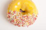 Freshly baked glazed orange ring donut or doughnut decorated with multicolored sprinkles viewed from above on white