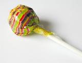 Close-up of a delicious lollipop or lolly wrapped in colorful plastic, with white stick, with copy space on grey