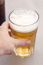 Man reaching for a glass of refreshing cold beer with a frothy head , high angle close up of his hand
