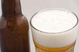 Bottled beer in a glass with a good frothy head viewed close up with the brown bottle alongside