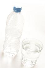 Bottled water served in a glass tumbler with the half full capped unlabeled plastic bottle alongside, high angle tilted view